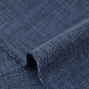 May include: A piece of dark navy blue fabric with a visible woven texture and a grid-like pattern. The material features a slightly frayed edge where it has been cut, showing the loose threads along the border of the folded textile surface.