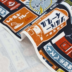 May include: A dark navy blue fabric featuring a repeating pattern of vintage-style Japanese signs and advertisements in orange, white, and light blue. The print includes various rectangular labels with Japanese text, illustrations of bottles, and coffee shop motifs.