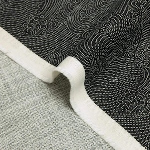 May include: A piece of fabric featuring a black background with a white dotted wave pattern. The fabric has a thick, off-white finished edge and a light gray, textured reverse side visible where the material is folded over to show both sides.