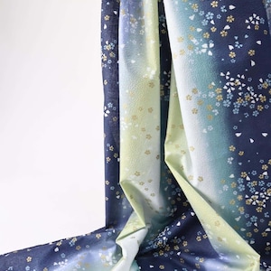 May include: A draped fabric with a gradient of colors, transitioning from deep navy to light blue and pale green. The fabric is adorned with a delicate floral pattern in white and gold, creating a serene and elegant aesthetic.