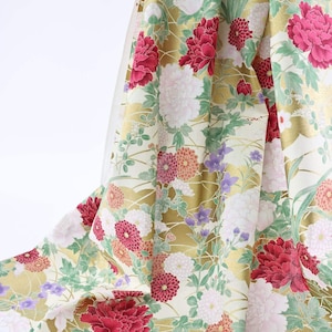 May include: A close-up of a fabric with a floral pattern. The fabric features large red and white peony flowers, smaller pink and orange blooms, and green foliage against a gold and cream background. The fabric is draped.