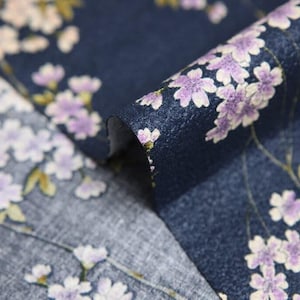 May include: Close-up of a navy blue fabric with a floral pattern. The design features delicate white and lavender blossoms with yellow-green leaves. The fabric is folded, revealing its texture and the intricate details of the print.