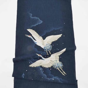 May include: Dark navy textile featuring two white cranes in flight, with red accents on their heads and blue detailing on their wings. The background includes stylized clouds and scattered white dots, suggesting a night sky.