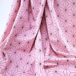 May include: Pink fabric with a repeating geometric pattern of dark brown lines. The fabric is draped, showing folds and shadows that highlight the design. The pattern consists of star-like shapes.
