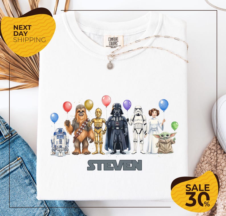 A white t-shirt with a graphic design featuring various characters from the Star Wars franchise, including Chewbacca, Darth Vader, Stormtrooper, and the character Steven. The characters are holding balloons, and the text "STEVEN" is displayed below the image.