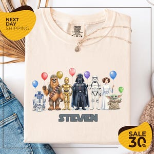 a t-shirt with a graphic design of various Star Wars characters, including Chewbacca, Darth Vader, Stormtrooper, and Yoda, along with balloons.