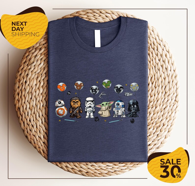 A blue t-shirt with a graphic design featuring various Star Wars characters, including Chewbacca, Stormtrooper, Baby Yoda, and Darth Vader, arranged in a row.