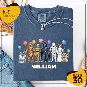 A t-shirt with a graphic design featuring various characters from the Star Wars franchise, including Chewbacca, Darth Vader, and the characters Baby Yoda, along with colorful balloons. The t-shirt is displayed on a white background, and there are yellow and black sale signs indicating a 30% discount.