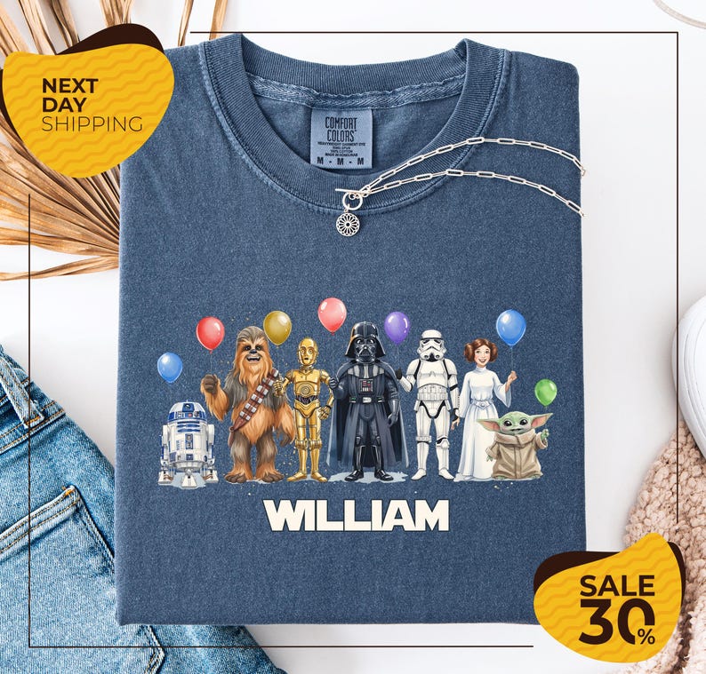 A t-shirt with a graphic design featuring various characters from the Star Wars franchise, including Chewbacca, Darth Vader, and the characters Baby Yoda, along with colorful balloons. The t-shirt is displayed on a white background, and there are yellow and black sale signs indicating a 30% discount.