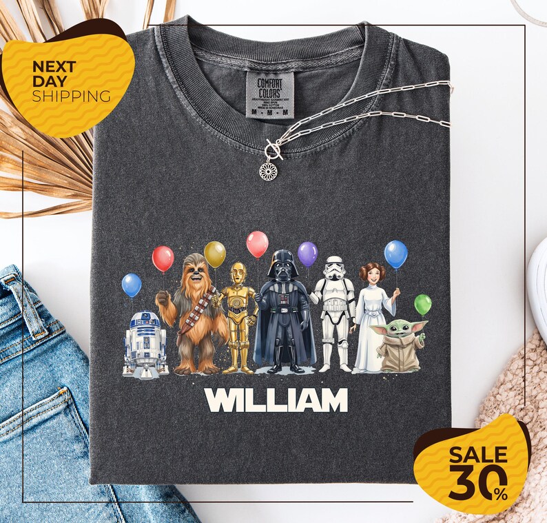A t-shirt with a graphic design featuring characters from the Star Wars franchise, including Chewbacca, Darth Vader, Stormtrooper, and Yoda, along with colorful balloons. The text "William" is displayed below the characters, and there are two yellow sale signs indicating a 30% discount on the t-shirt.