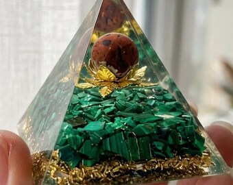 May include: A clear resin pyramid containing a base layer of gold metal shavings, a thick middle layer of crushed green malachite stones, and a single brown spotted sphere resting on a small gold-colored metal leaf-shaped decorative element.