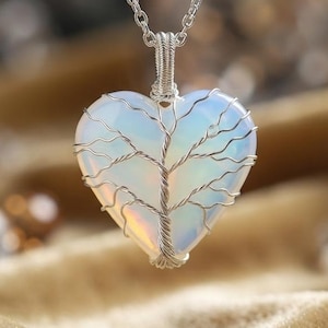 May include: A heart-shaped pendant necklace featuring a translucent, iridescent stone wrapped in silver-coloured wire. The wire is intricately twisted across the surface of the heart to resemble the branches and trunk of a tree, suspended by a chain.