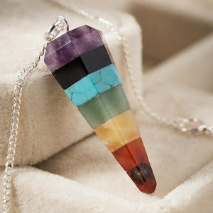 May include: A multi-colored, faceted, cone-shaped pendant hanging from a silver-toned metal chain. The pendant is composed of seven stacked horizontal layers of different colored stones, including purple, black, turquoise, green, yellow, orange, and red.