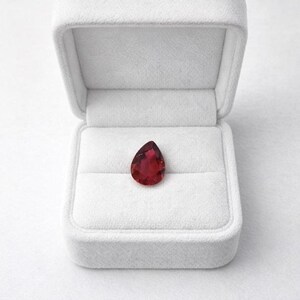 Genuine red ruby faceted pear cut gemstone close view showing natural inclusions and sparkle, suitable for luxury jewelry making