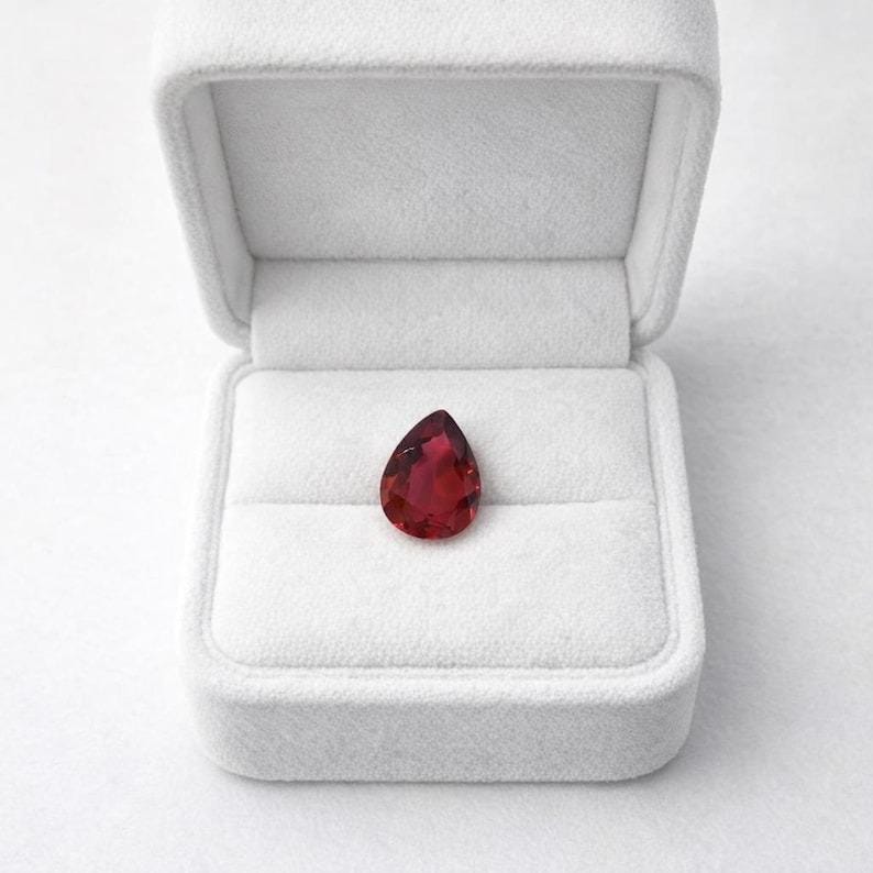 Genuine red ruby faceted pear cut gemstone close view showing natural inclusions and sparkle, suitable for luxury jewelry making