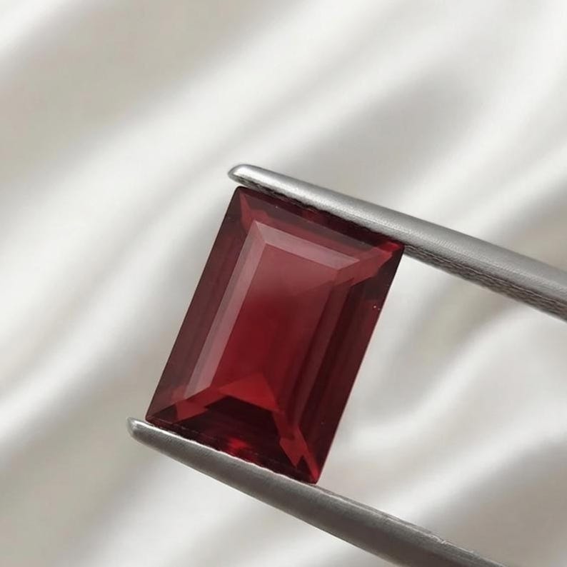 Close-up of a deep red ruby rectangular baguette gemstone with polished facets and clean step cut edges, perfect for luxury ring setting, wedding band design, and fine jewelry making supply.