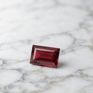Faceted red ruby rectangular gemstone with elegant baguette cut, showcasing glassy luster and deep color saturation, suitable for July birthstone jewelry and luxury custom jewelry settings.