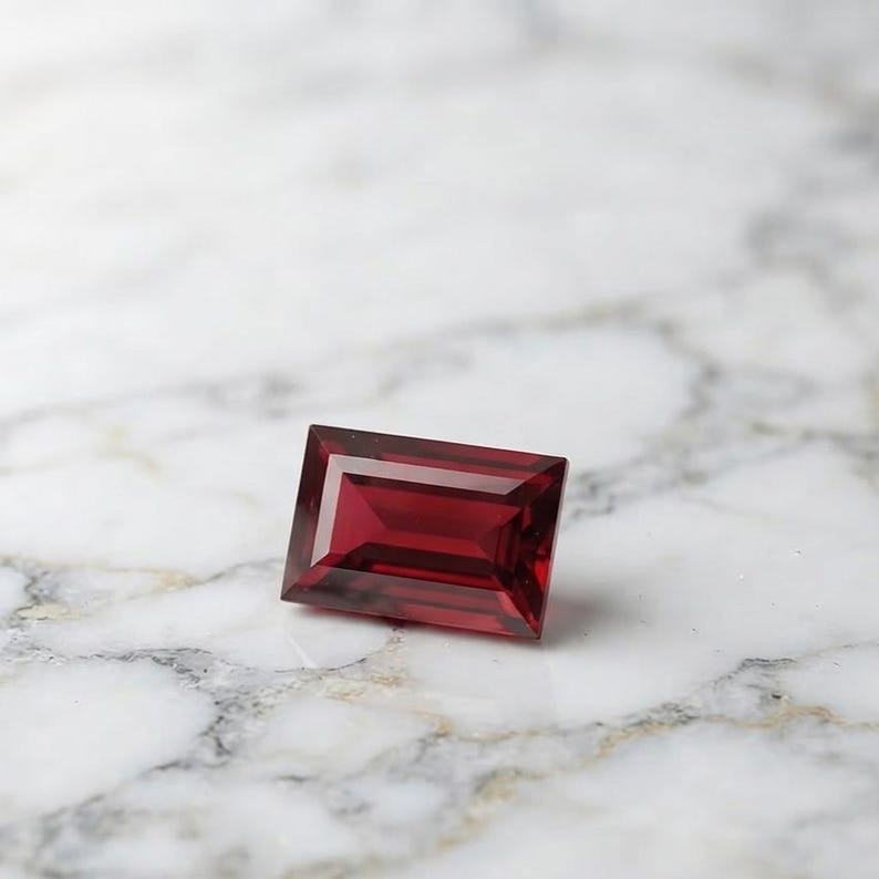Faceted red ruby rectangular gemstone with elegant baguette cut, showcasing glassy luster and deep color saturation, suitable for July birthstone jewelry and luxury custom jewelry settings.