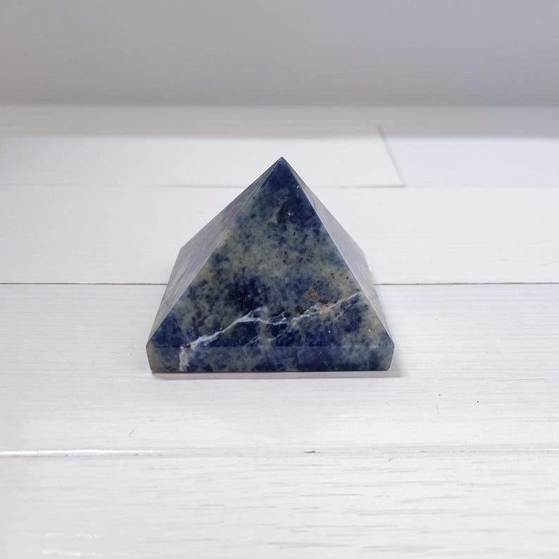 Healing sodalite crystal pyramid placed on wooden background, ideal for Reiki sessions and chakra balancing practices.