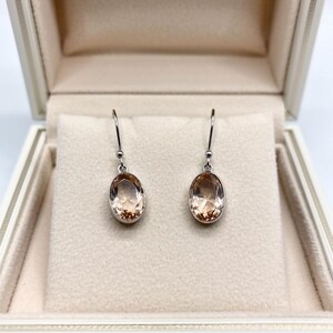 Close up of peach stone drop earrings in 925 sterling silver setting, elegant oval crystal jewelry accessory perfect for bridal shower, engagement party or formal evening wear.