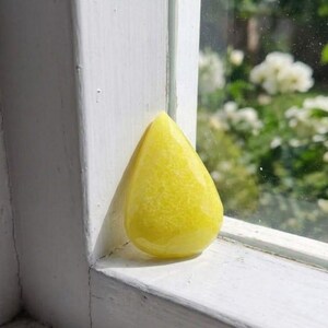Golden yellow sapphire rough pear shaped gem resting on satin background, natural healing crystal for prosperity, meditation altar decor, and jewelry design supply.