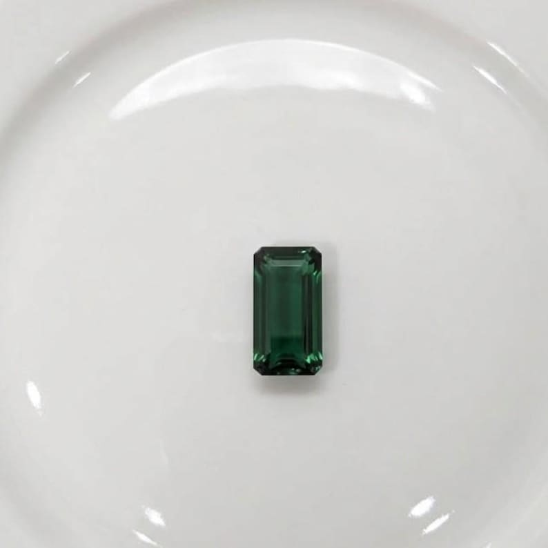 Deep green natural emerald gemstone in emerald cut shape shown as loose stone for ring setting, fine jewelry design, luxury engagement ring centerpiece and May birthstone crystal gift.