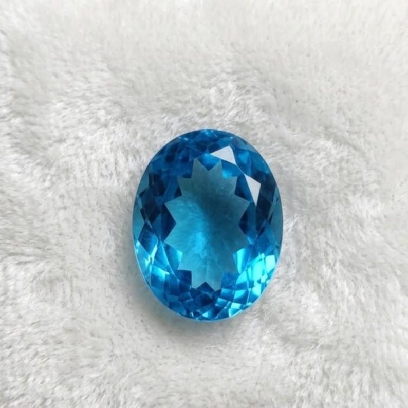Fine quality Swiss Blue Topaz oval cut gemstone displayed as loose precious stone for custom engagement ring and luxury handmade jewelry designs.