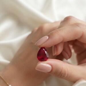 Faceted red ruby pear cut loose stone displayed in tweezers highlighting clarity and rich color, ideal for luxury engagement ring or fine jewelry creation