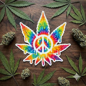 May include: A colorful tie-dye cannabis leaf sticker with a white peace sign in the center. The sticker has a dripping effect and is surrounded by green cannabis leaves and buds on a wooden surface.