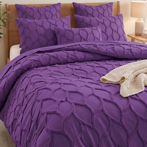 Puede incluir: Un juego de cama de color morado vibrante con un patrón de celosía texturizado y en relieve en la funda nórdica y las fundas de almohada a juego. Una manta de punto de color crema está colocada a los pies de la cama, añadiendo textura.