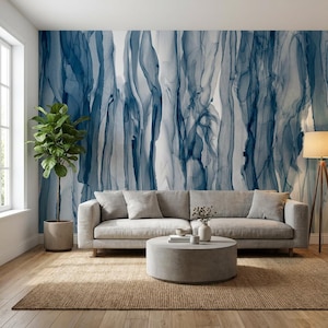 May include: A modern living room featuring a gray sofa, a round concrete coffee table, and a jute rug. The focal point is a wall mural with abstract blue and white ink-like patterns. A potted plant and a floor lamp add to the decor.