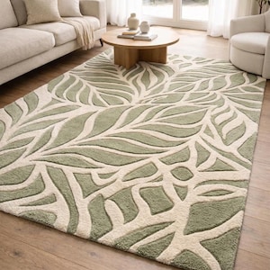 May include: A large rectangular rug featuring a leaf design in green and cream. The rug is placed on a wooden floor and is surrounded by furniture, including a sofa and chairs. The leaf pattern adds a natural touch to the room's decor.