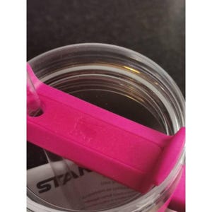 May include: A clear glass jar with a bright pink lid and handle. The jar has a wide mouth and a screw-on lid. The lid has a rectangular handle with a small logo. The jar is partially filled.