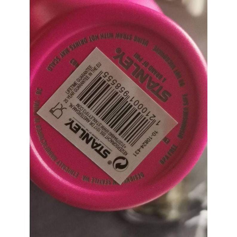 May include: A close-up of a pink Stanley brand tumbler base. The base has the brand name and product information printed on it. The label includes a barcode, a lifetime guarantee, and BPA-free information.
