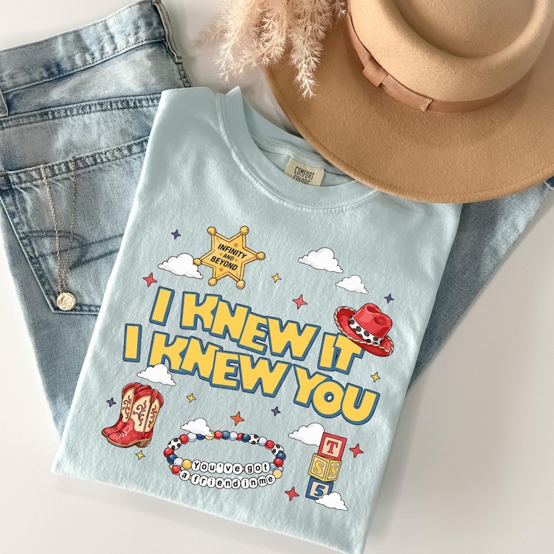 May include: A light blue t-shirt featuring the yellow text I KNEW IT I KNEW YOU, a gold sheriff star with the text INFINITY AND BEYOND, a red cowboy hat, red cowboy boots, a beaded bracelet with the text YOU'VE GOT A FRIEND IN ME, and blocks.