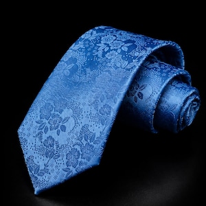 Peut inclure: Une cravate bleu vif ornée d'un motif floral ton sur ton avec des détails botaniques complexes et une finition légèrement texturée. La cravate est partiellement enroulée, mettant en valeur la construction du tissu tissé et la couleur bleue uniforme.