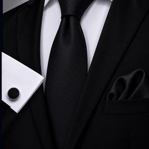 Peut inclure: Une cravate noire avec un motif géométrique carré subtil, une pochette assortie et un bouton de manchette rond avec une incrustation noire à motif carré, portés avec une chemise blanche et une veste de costume noire pour un ensemble formel.