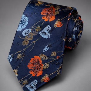 May include: A navy blue necktie featuring a woven floral pattern with vibrant orange, light blue, and metallic gold thread details. The fabric has a smooth, slightly reflective finish, and the tie is partially rolled at the top, displaying the pattern.