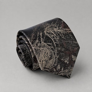 May include: A rolled necktie in a dark charcoal black color featuring a light beige and muted brown botanical print. The pattern consists of fine, intricate line drawings of leaves, stems, and floral elements scattered across the fabric surface.
