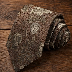 May include: A necktie featuring a dark brown base with a textured finish and a repeating pattern of light gray and muted green floral motifs, including detailed leaves and blossoms, arranged in a dense, intricate botanical design across the fabric.
