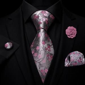 Könnte beinhalten: Ein schwarzes Anzug- und Hemd-Set mit einer silbergrauen Krawatte und einem passenden Einstecktuch mit rosa Blumenmuster. Das Set enthält einen runden silbergrauen Manschettenknopf mit rosa Blumenmuster und eine Ansteckblume aus rosa Stoff.