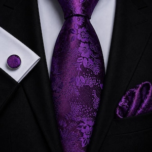 Könnte beinhalten: Eine tiefviolette Krawatte mit einem tonalen Blumenmuster, kombiniert mit einem passenden violetten Einstecktuch und einem runden Manschettenknopf mit violetter Blumeneinlage, getragen zu einem weißen Hemd und einem schwarzen Sakko.