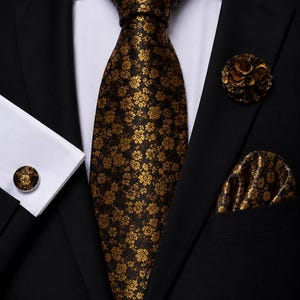 Può includere: Una giacca da abito nera con camicia bianca, cravatta con motivo floreale nero e oro, pochette abbinata, una spilla da bavero floreale rotonda e un gemello circolare con lo stesso motivo floreale nero e oro sulla manica.