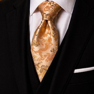 Peut inclure: Gros plan d'une cravate dorée avec un motif floral et de dragon complexe. La cravate est nouée et portée avec une chemise blanche à col et une veste de costume noire. La pochette est blanche.