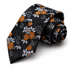 May include: A black necktie featuring a repeating floral pattern with orange and light grey blossoms, accented by small white star-like clusters. The fabric has a subtle, intricate tonal texture throughout the background of the tie.
