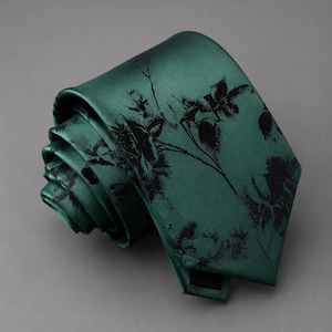 Op de afbeelding: Een donker smaragdgroene das met een zwarte bloemenprint in silhouet. De das is opgerold tot een spiraal en toont een gladde, satijnachtige afwerking en een puntig uiteinde. Het donkere botanische patroon contrasteert met de diepgroene stof.