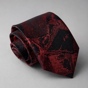 May include: A necktie featuring a dark red and black abstract pattern with a textured, woven appearance. The tie is rolled into a coil, displaying the pointed end and the intricate, dark, organic shapes woven into the deep red fabric surface.