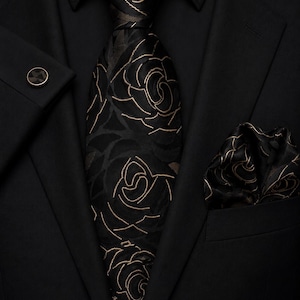 May include: A formal outfit comprising a black suit, shirt, tie, pocket square, and cufflink. The tie and pocket square showcase a gold floral pattern on a black backdrop. The cufflink is gold.