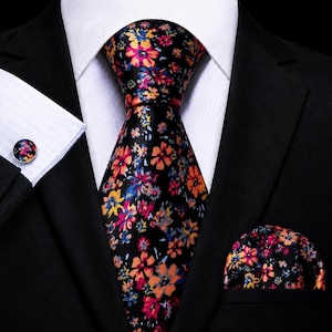 Peut inclure: Un ensemble composé d'une cravate, d'une pochette et de boutons de manchette noirs, ornés d'un motif floral aux teintes vives de rose, orange, jaune et bleu. Les accessoires sont présentés sur une chemise blanche et une veste de costume noire.