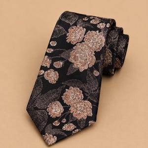 May include: A black necktie featuring a woven floral pattern in shades of copper and muted brown. The design displays detailed blossoms and leaves distributed across the fabric, with the tie folded at the top to show its layered construction.